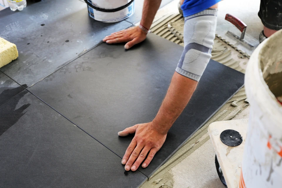 Artisan posant du carrelage gris anthracite sur chape ciment avec adhésif