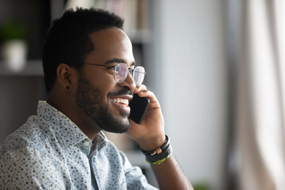 Souriant jeune adulte afro-américain homme d'affaires hipster professionnel faisant un appel téléphonique professionnel parlant au téléphone au bureau jouant d'une conversation d'entreprise mobile à l'intérieur, vue de profil en gros plan