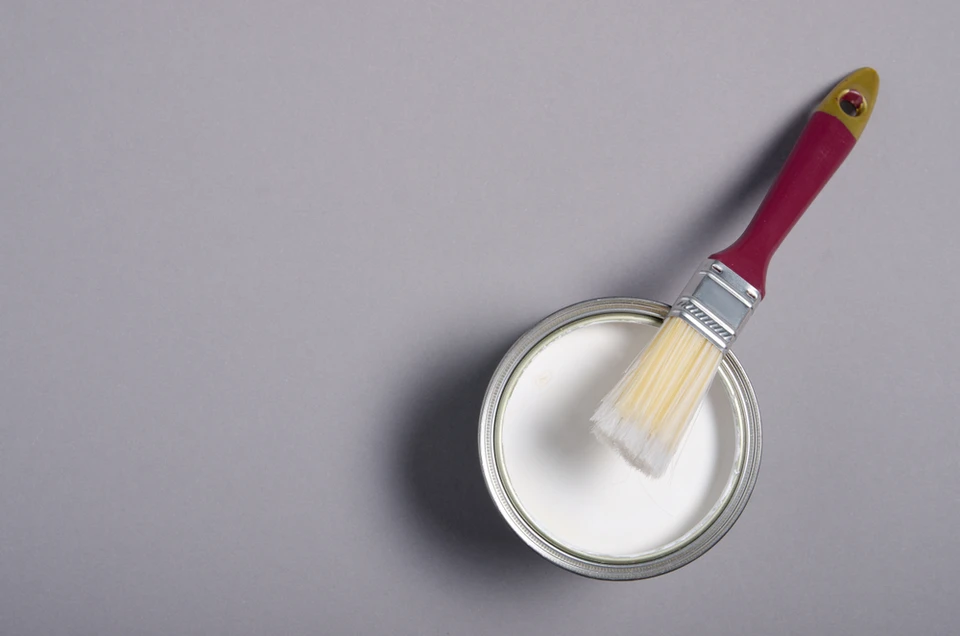 Scène d'intérieur sur fond neutre présentant un pot de peinture ouvert avec pinceau posé en travers