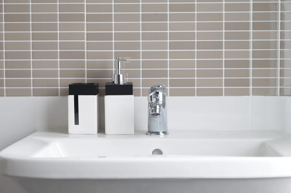 Salle de bain moderne avec carrelage beige à motifs géométriques, lavabo blanc encastré dans meuble en bois, miroir avec étagère, plantes vertes décoratives, serviettes blanches pliées, accessoires de toilette turquoise