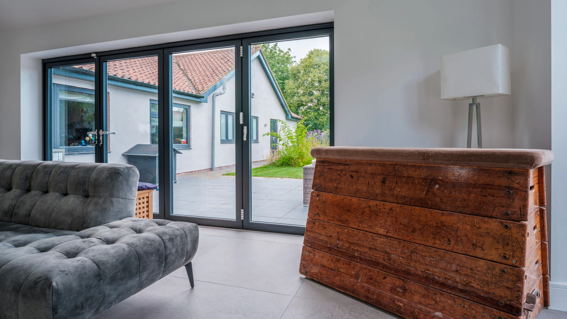 Gros plan sur une fenêtre PVC ou aluminium blanc fraîchement installée, cadre des menuiseries visible depuis l'intérieur d'une pièce rénovée. La fenêtre ouvre sur un extérieur verdoyant naturel et lumineux. Dans le cadre intérieur, on voit le rebord lisse et la quincaillerie chromée moderne de la poignée. Le mur autour montre une finition peinte récente de qualité. L'image transmet confort, luminosité et travail de qualité réalisé.